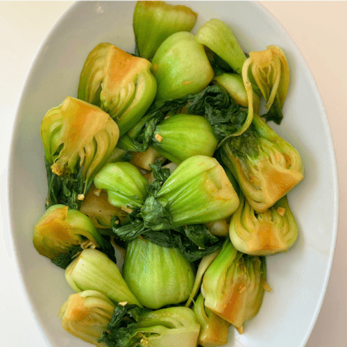 Baby bok choy stir fried with minced garlic and ginger in a white bowl