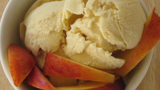 peaches and cream ice cream in a bowl and garnished with fresh peaches