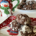 chocolate crinkle cookies on a snowman plate with a snowman cup in the background and a large plate of cookies in the background