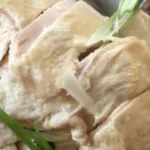 close up of chopped up chicken with green onion garnishes on a platter