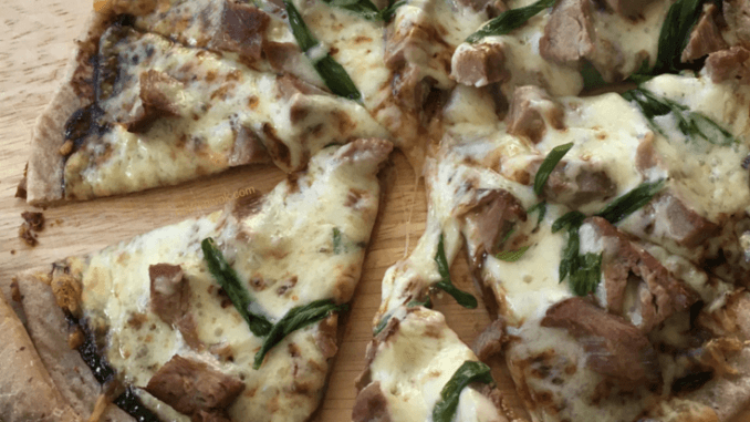 Smoked Duck with Hoisin Sauce Pizza on a wooden cutting board, with two fingers holding one slice