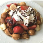 Bubble Egg Waffle Sundae piled high with ice cream, sliced strawberries, whipped cream, and chococlate sauce drizzle. #nutfree #dessert