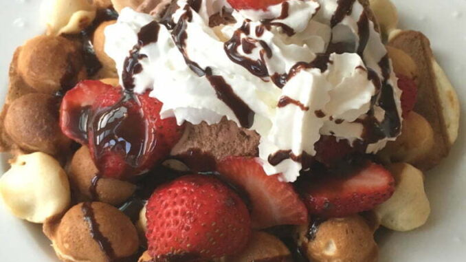 Bubble Egg Waffle Sundae piled high with ice cream, sliced strawberries, whipped cream, and chococlate sauce drizzle. #nutfree #dessert