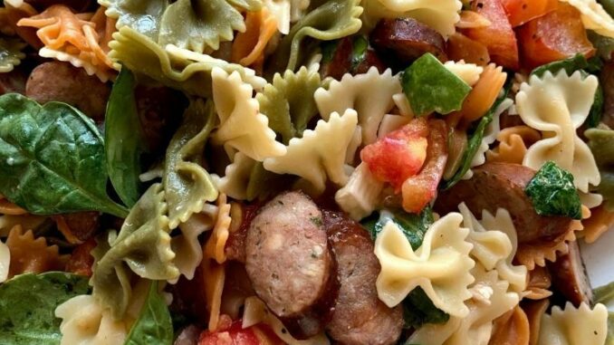 a platter of rainbow bowtie pasta with tomatoes, brie, and sausages