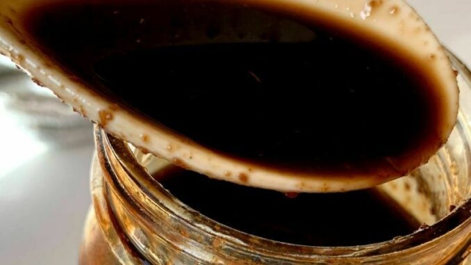 Close up of teriyaki sauce in a spoon with a jar of sauce.