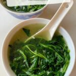 two bowls of watercress and garlic soup in a white soup bowl with white Chinese soup spoons