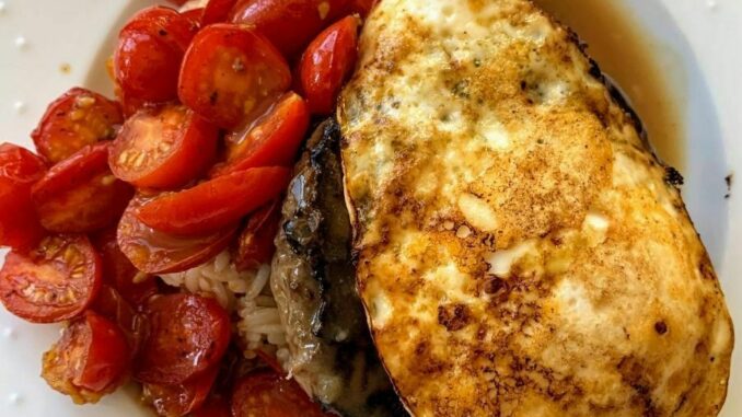 Rice topped with hamburger patty, gravy, egg, and tomatoes on a white plate.