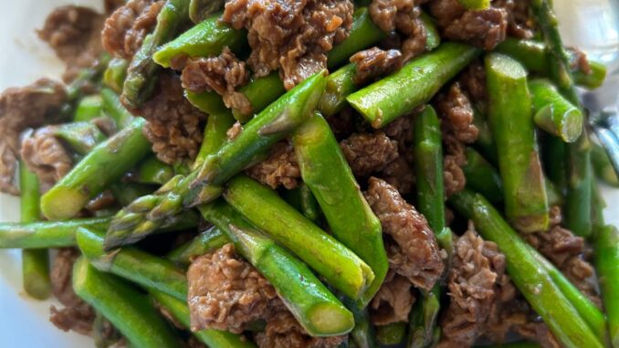 Asparagus stir fried with beef in a white serving plate.