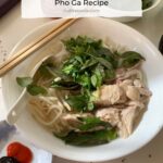 Close up of chicken, herbs, chicken broth, and rice noodles in a white bowl