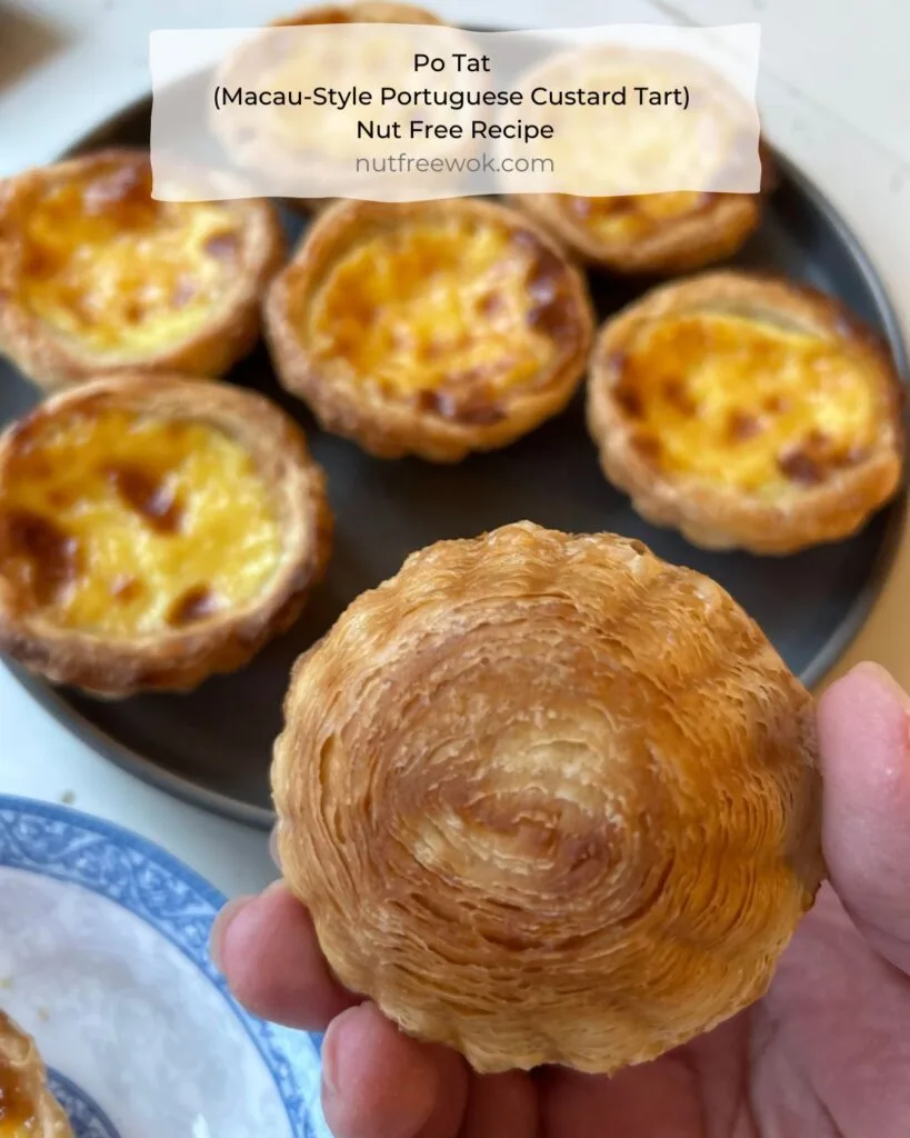 close up of the bottom of an egg tart with a swirly puff pastry crust, background has a plate of po tats