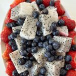dragon fruit salad with blueberries, strawberries, and watermelon arranged in a white oval serving bowl.
