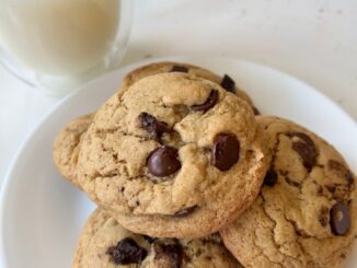 a pile of olive oil chocolate chip cookies on a white plate, next to a glass of milk
