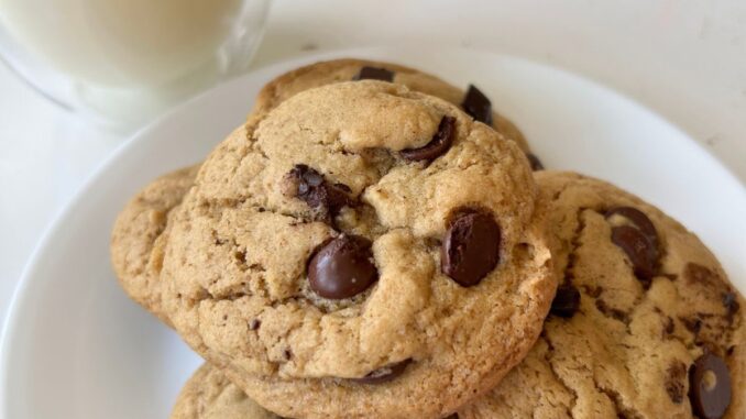 a pile of olive oil chocolate chip cookies on a white plate, next to a glass of milk