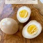 close up of a whole ramen egg and a ramen egg cut in half on a wooden cutting board