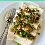 cold tofu topped with sesame oil, soy, and scallions are served in a white bowl