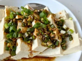 cut pieces of cold tofu, topped with soy sauce, sesame and scallion dressing, served in a white bowl