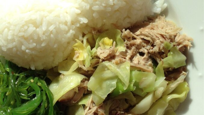 overhead image of kalua pork and cabbage plate with rice and seaweed salad in a white plate