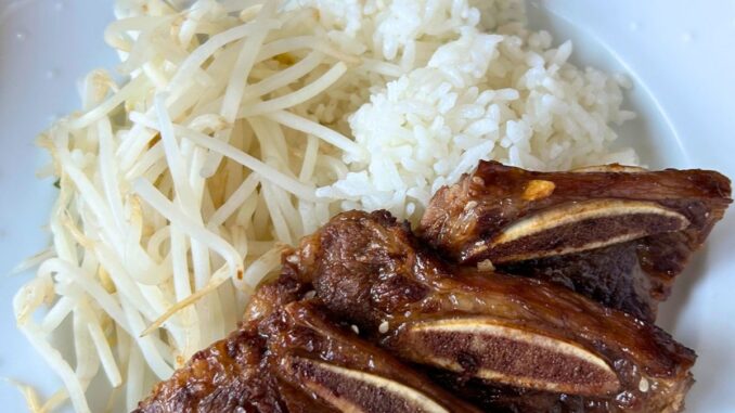Plate of Korean style beef short ribs with rice and cooked mung bean sprouts.