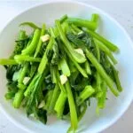 yu choy stir fried with garlic served in a round white serving bowl