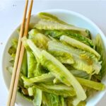 stir-fried romaine lettuce in a white serving bowl with chopsticks on the left