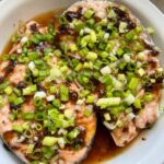 steamed salmon steaks with black bean garlic sauce and topped with scallions in a white serving dish