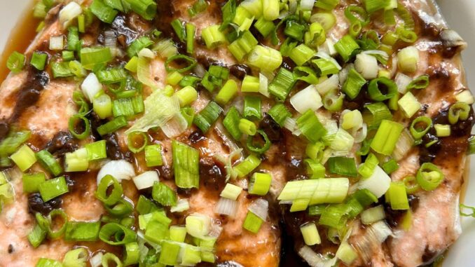 steamed salmon steaks with black bean garlic sauce and topped with scallions in a white serving dish