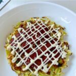 Okonomiyaki with turkey bacon, served with sauce and a drizzle of mayonaise in a criss-cross pattern.