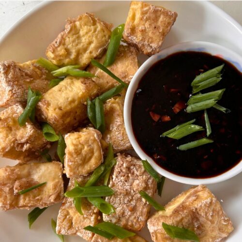 golden brown and crispy air fryer tofu bites served on a round white plate with a dip on the side