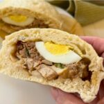 A dai bao cut in half to show the filling ingredients (egg, chicken, sausage, and pork encased with a fluffy steamed bread.